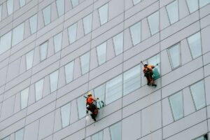 Two workers wear harnesses while washing the windows of a skyscraper.